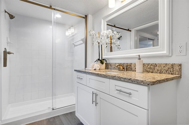 full bathroom featuring a stall shower, vanity, a textured ceiling, and wood finished floors