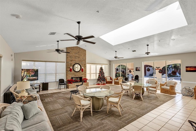 tiled dining space featuring a textured ceiling, vaulted ceiling with skylight, a fireplace, and visible vents