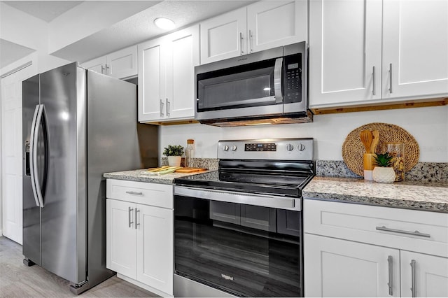 kitchen with stainless steel appliances, light wood-type flooring, white cabinetry, and light stone countertops