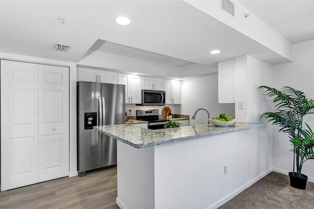 kitchen with light stone counters, stainless steel appliances, visible vents, white cabinetry, and a peninsula