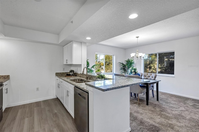 kitchen with white cabinets, light stone counters, a peninsula, stainless steel dishwasher, and a sink