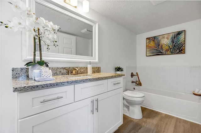 bathroom with a textured ceiling, a garden tub, toilet, wood finished floors, and vanity