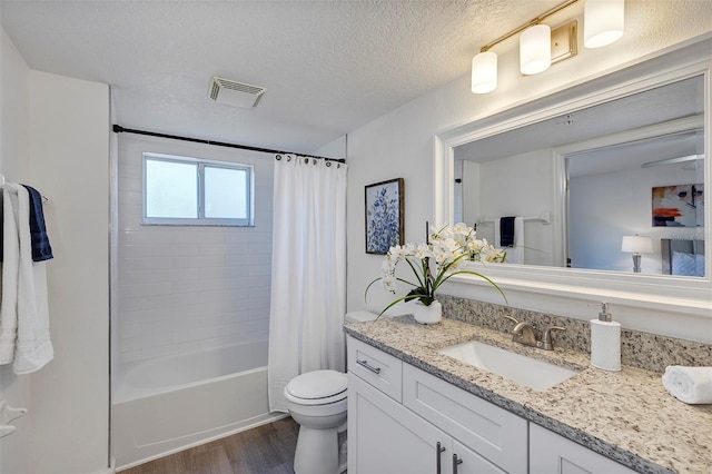 full bathroom with a textured ceiling, toilet, wood finished floors, vanity, and visible vents