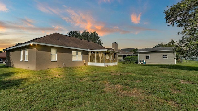 back house at dusk featuring a yard and a sunroom