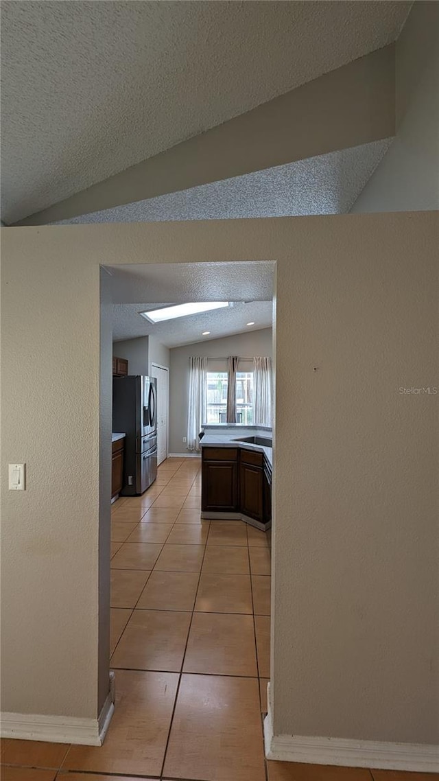 corridor featuring vaulted ceiling with skylight, a textured ceiling, and light tile patterned flooring