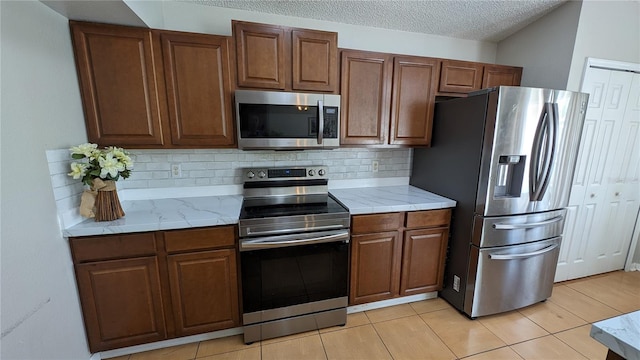 kitchen featuring a textured ceiling, appliances with stainless steel finishes, light tile patterned floors, and decorative backsplash