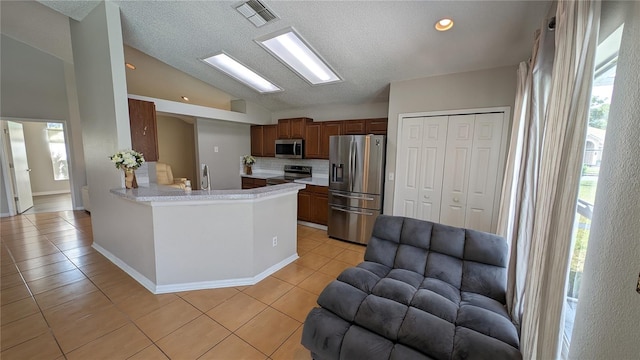 kitchen featuring lofted ceiling, kitchen peninsula, decorative backsplash, appliances with stainless steel finishes, and light tile patterned floors