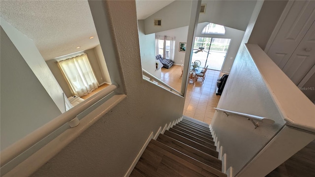 staircase featuring vaulted ceiling, a textured ceiling, and hardwood / wood-style flooring