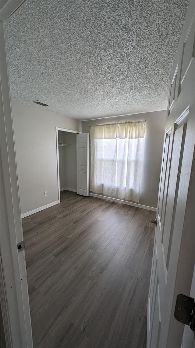 unfurnished bedroom featuring a textured ceiling, a closet, and dark hardwood / wood-style floors