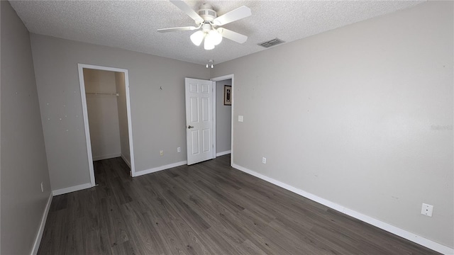 unfurnished bedroom featuring a closet, a textured ceiling, dark hardwood / wood-style floors, a spacious closet, and ceiling fan