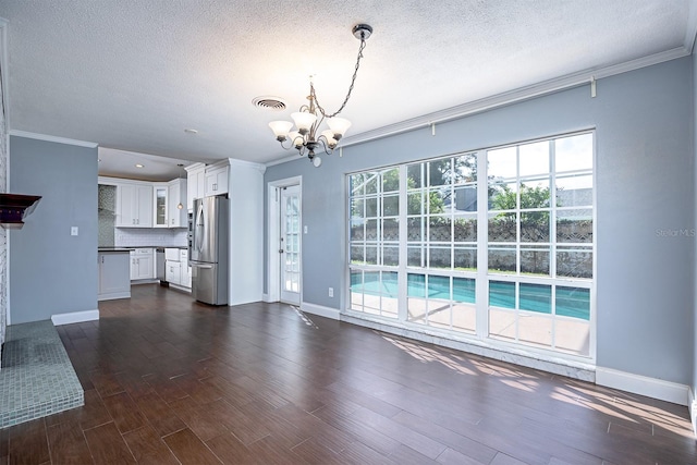 unfurnished living room featuring a textured ceiling, crown molding, dark wood-type flooring, and a notable chandelier