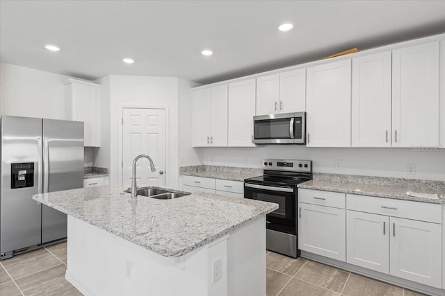 kitchen with an island with sink, light stone counters, stainless steel appliances, sink, and white cabinetry