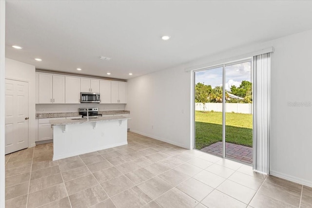 kitchen featuring an island with sink, light stone countertops, white cabinets, light tile patterned flooring, and appliances with stainless steel finishes