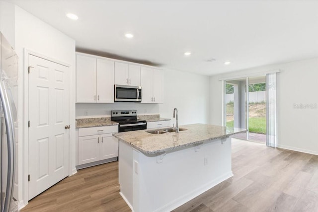 kitchen with light wood-type flooring, sink, an island with sink, white cabinets, and stainless steel appliances