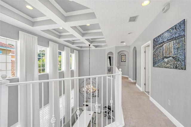 corridor featuring crown molding, coffered ceiling, an inviting chandelier, beam ceiling, and light colored carpet