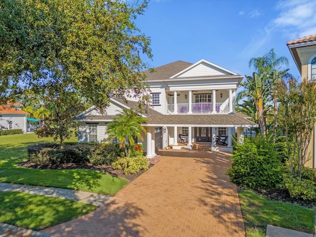 neoclassical home with a balcony, a front lawn, and covered porch