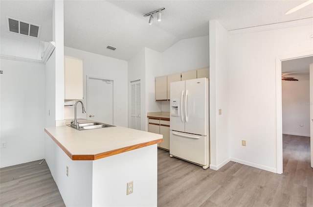 kitchen featuring vaulted ceiling, white refrigerator with ice dispenser, kitchen peninsula, light wood-type flooring, and sink