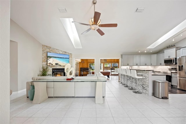 tiled living room featuring ceiling fan, a fireplace, and lofted ceiling with skylight