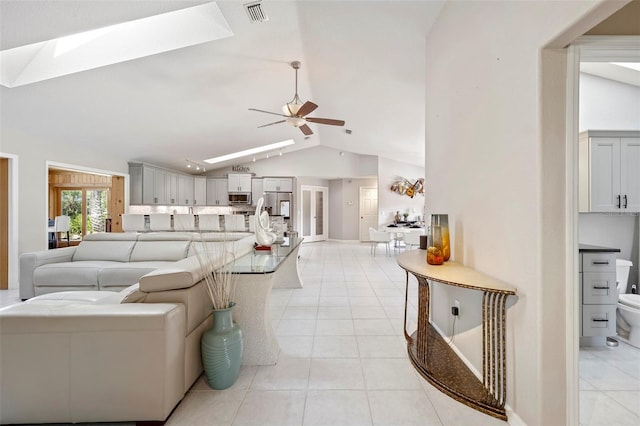 tiled living room with ceiling fan and vaulted ceiling with skylight