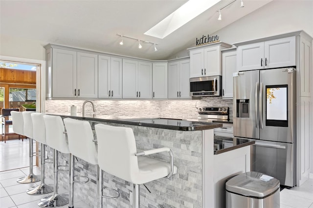 kitchen with stainless steel appliances, lofted ceiling with skylight, tasteful backsplash, and a breakfast bar