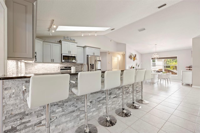 kitchen featuring gray cabinets, backsplash, appliances with stainless steel finishes, light tile patterned floors, and lofted ceiling with skylight