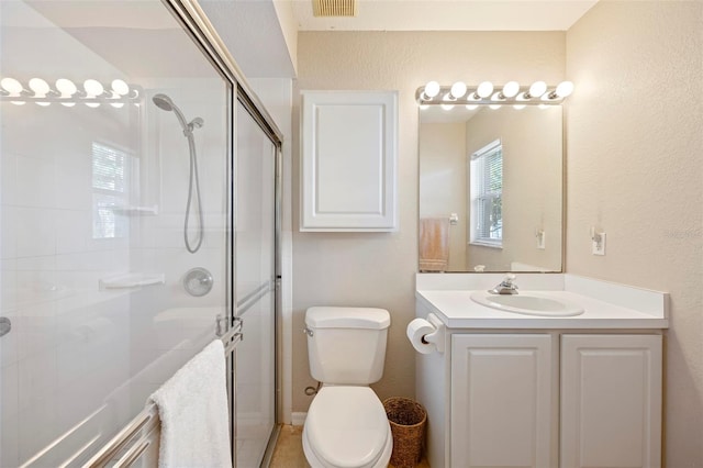 bathroom with a shower with shower door, plenty of natural light, vanity, and toilet