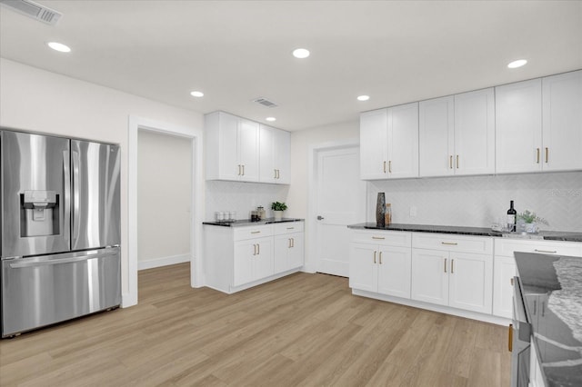 kitchen with light hardwood / wood-style flooring, dark stone countertops, stainless steel refrigerator with ice dispenser, and white cabinetry