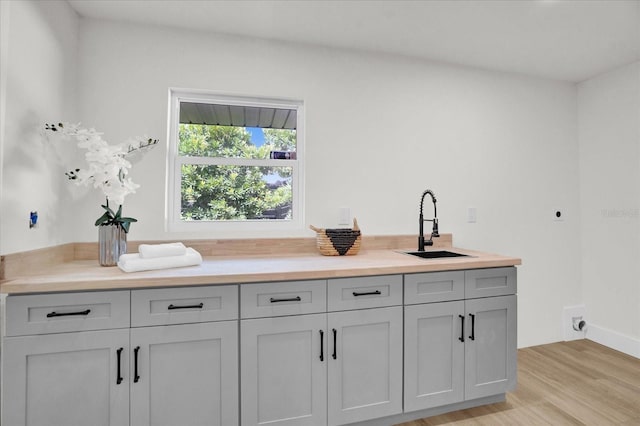 bar with light hardwood / wood-style flooring, gray cabinets, and sink