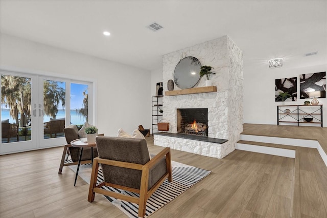 living room with wood-type flooring, a stone fireplace, and french doors