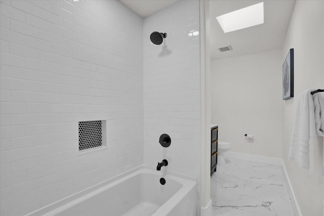 bathroom with a skylight, tiled shower / bath combo, and toilet