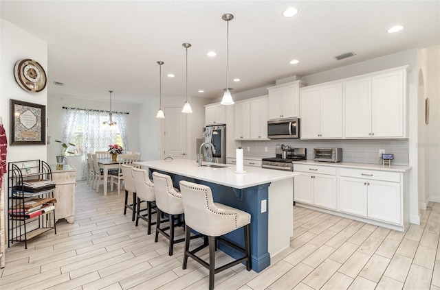 kitchen with appliances with stainless steel finishes, sink, pendant lighting, a center island with sink, and white cabinetry