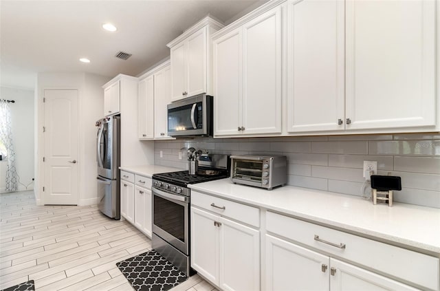 kitchen with tasteful backsplash, white cabinetry, light hardwood / wood-style flooring, and stainless steel appliances