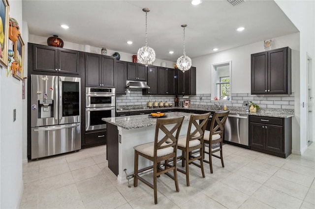 kitchen featuring decorative light fixtures, appliances with stainless steel finishes, a kitchen breakfast bar, a kitchen island, and light stone countertops