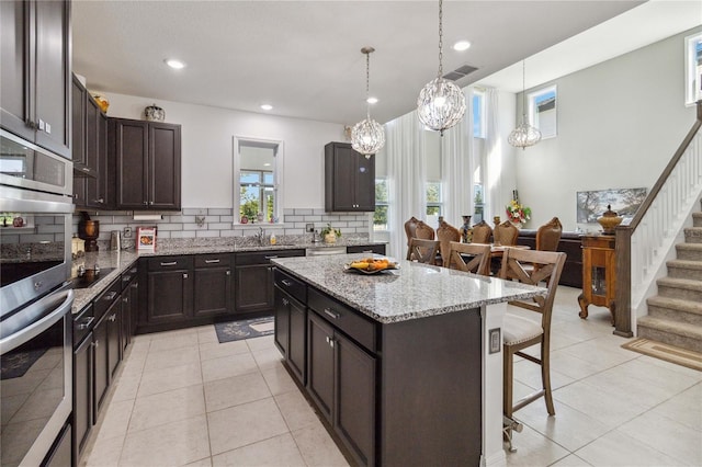 kitchen featuring a kitchen bar, dark brown cabinets, light tile patterned floors, a kitchen island, and decorative backsplash