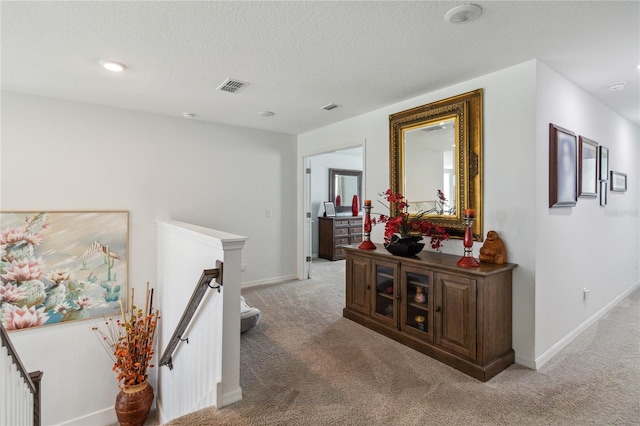 hall featuring light carpet and a textured ceiling