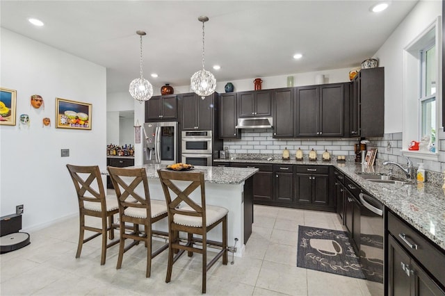 kitchen featuring sink, a breakfast bar, stainless steel appliances, a center island, and light stone counters