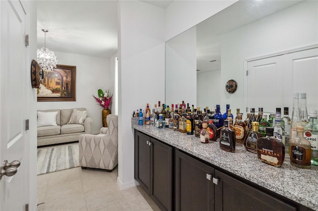 bar featuring hanging light fixtures, light tile patterned floors, a notable chandelier, dark brown cabinetry, and light stone counters