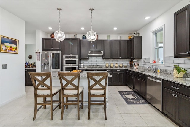 kitchen with appliances with stainless steel finishes, a kitchen breakfast bar, a kitchen island, pendant lighting, and light stone countertops