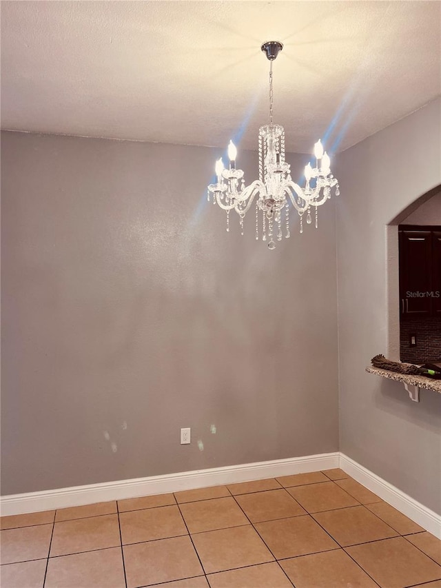 spare room with a textured ceiling, a chandelier, and tile patterned floors