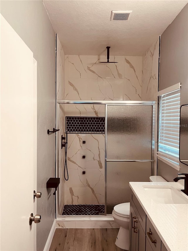 bathroom featuring wood-type flooring, a textured ceiling, a shower with shower door, vanity, and toilet