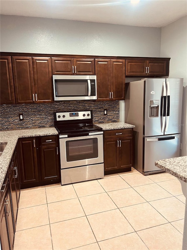 kitchen featuring dark brown cabinets, light tile patterned flooring, decorative backsplash, stainless steel appliances, and light stone countertops