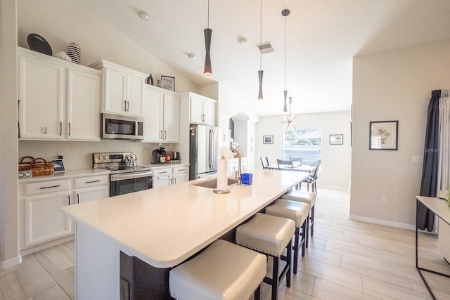 kitchen with pendant lighting, a kitchen island with sink, vaulted ceiling, white cabinetry, and appliances with stainless steel finishes