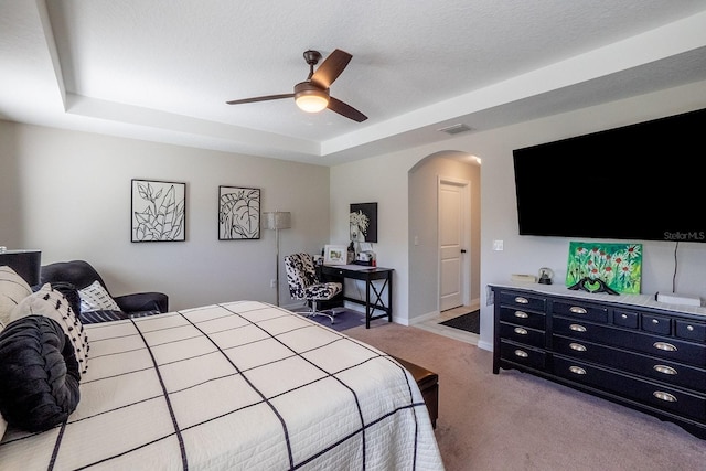 bedroom featuring light carpet, a tray ceiling, ceiling fan, and a textured ceiling