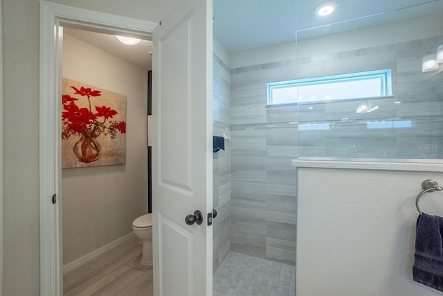 bathroom with wood-type flooring, tiled shower, and toilet