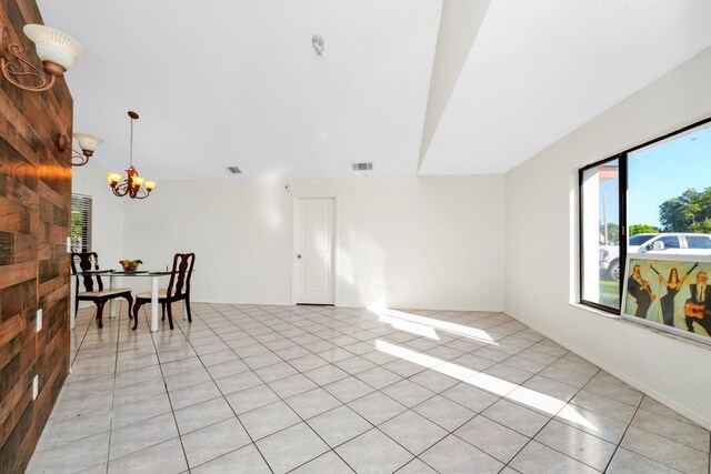 unfurnished room with a notable chandelier, wooden walls, and light tile patterned flooring