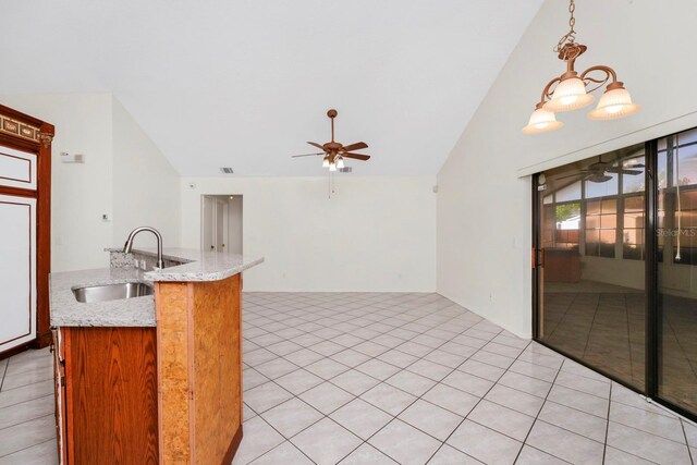 kitchen featuring light stone counters, light tile patterned flooring, hanging light fixtures, sink, and ceiling fan with notable chandelier