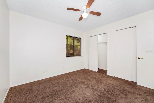 unfurnished bedroom featuring a textured ceiling, two closets, dark colored carpet, and ceiling fan