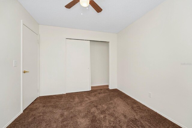 unfurnished bedroom with ceiling fan, a closet, and dark colored carpet