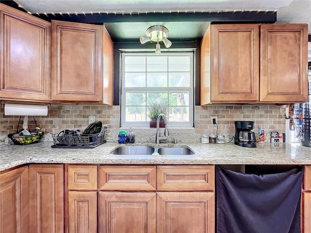 kitchen featuring black dishwasher, light stone counters, tasteful backsplash, and sink