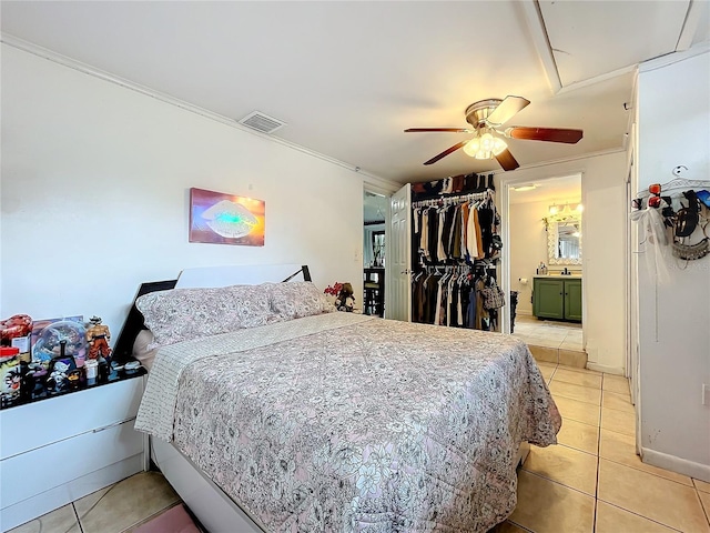 tiled bedroom featuring ornamental molding, ensuite bath, ceiling fan, and a closet